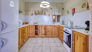 A kitchen with wooden cabinets, a white countertop, a stove, and a hanging light fixture. - Stone Apt in Nadur | Terrace & Patio | Sleeps 6 (Nadur)