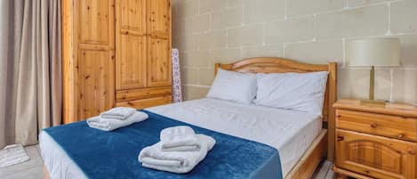 A bedroom with a bed, a wooden wardrobe, a nightstand, and a lamp.