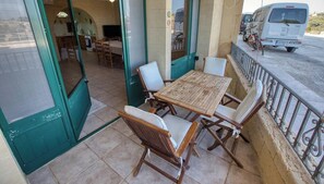 An outdoor dining area with a table and chairs, a view of the street, and a parked vehicle. - Stone Apt in Nadur | Terrace & Patio | Sleeps 6 (Nadur)