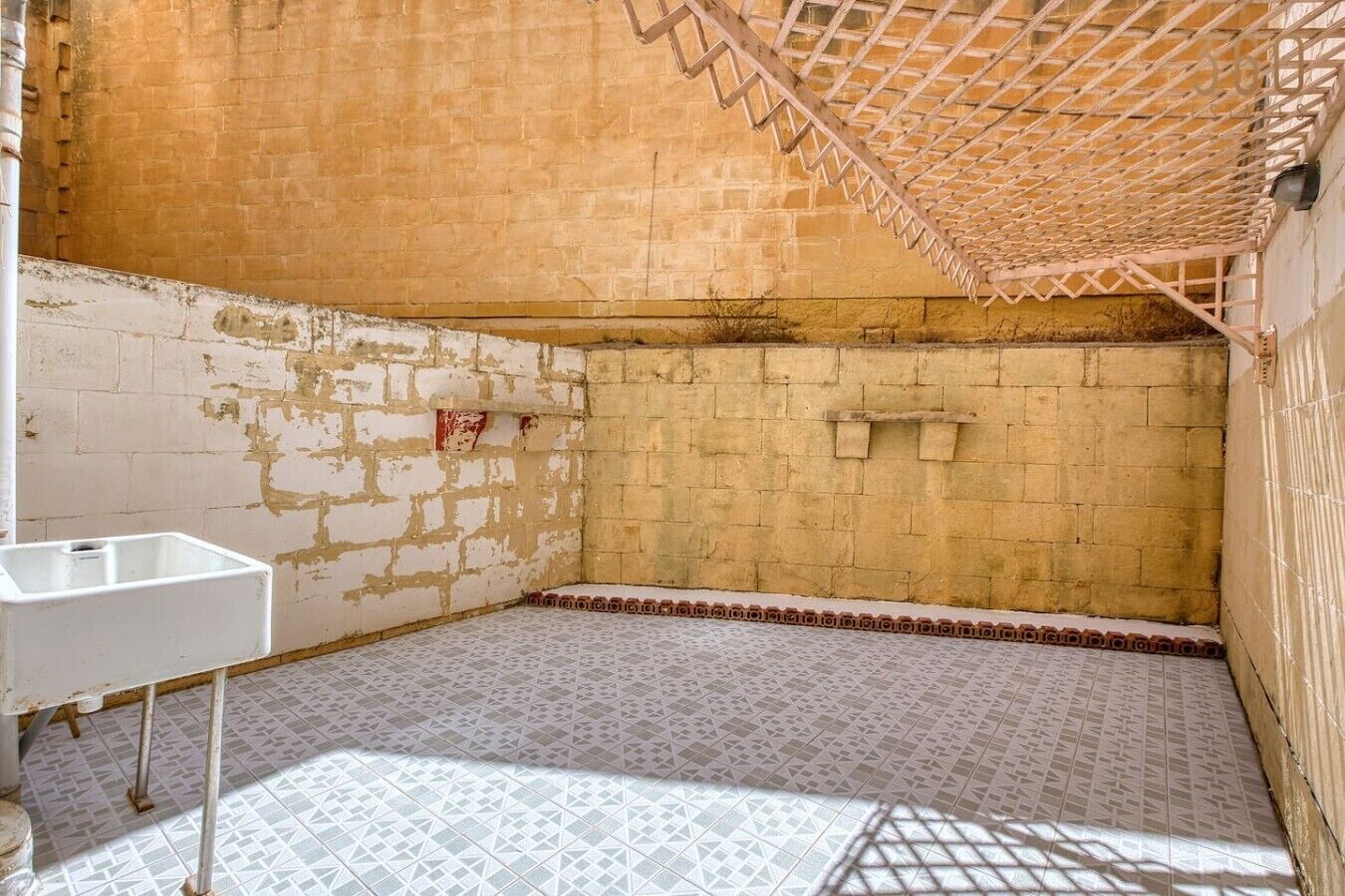 Une pièce avec un lavabo blanc, un sol à motifs et un mur en briques.