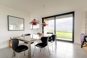 Een moderne eetruimte met een glazen tafel, zwarte stoelen en rode hanglampen.