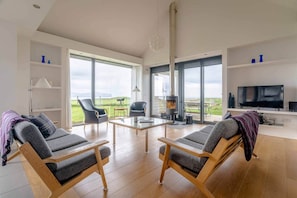 A spacious living room with a large window, a fireplace, a television, and a dining area. - The Two Byres, Isle of Skye (Isle of Skye)