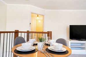 En matplats med ett träbord dukat för två personer, en tv på ett stativ och en dörr som leder till ett annat rum.