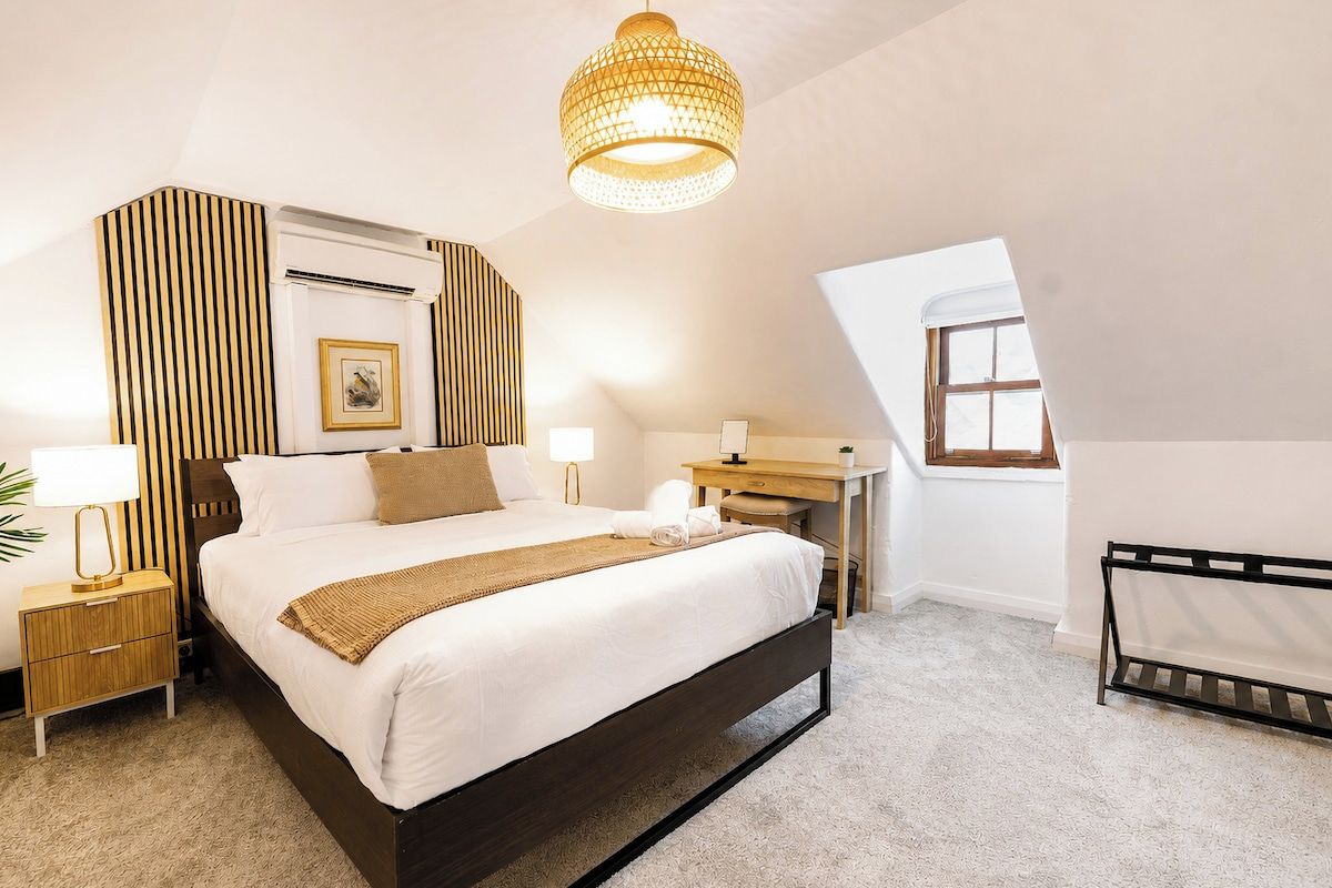 A modern bedroom with a large bed, bedside tables, a desk, and a hanging light fixture.