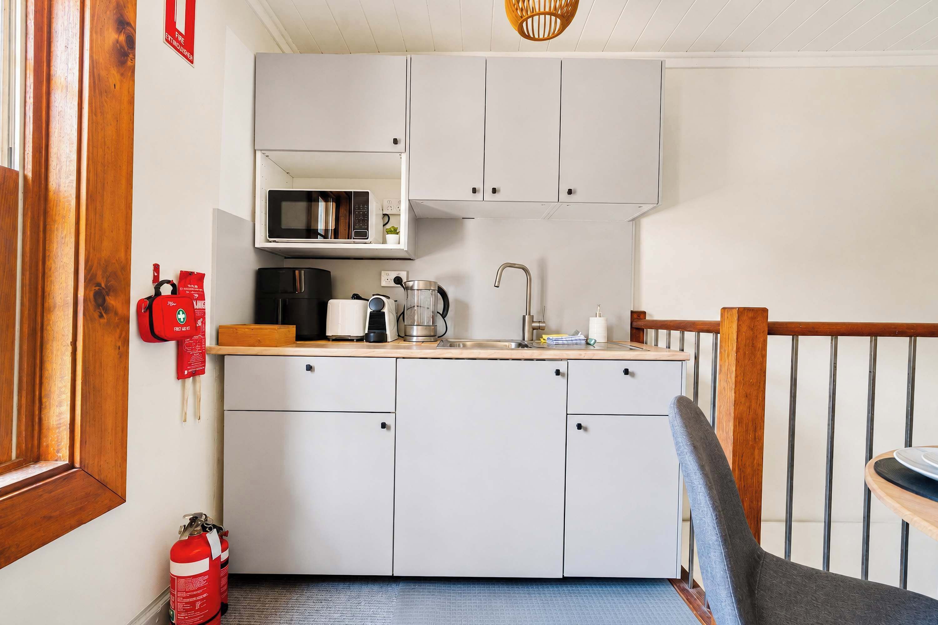 Cocina compacta con armarios blancos, microondas, hervidor de agua y cafetera.