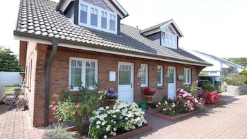 A two-story house with a tiled roof, brick walls, and a front garden with various flowers.