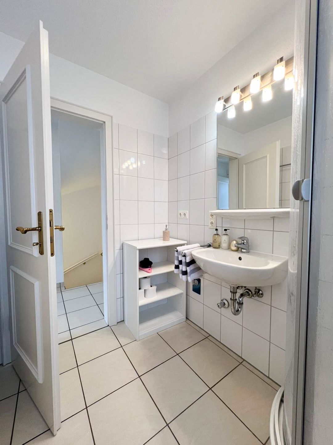 A bathroom with white tiles, a sink with overhead lights, and a towel rack.