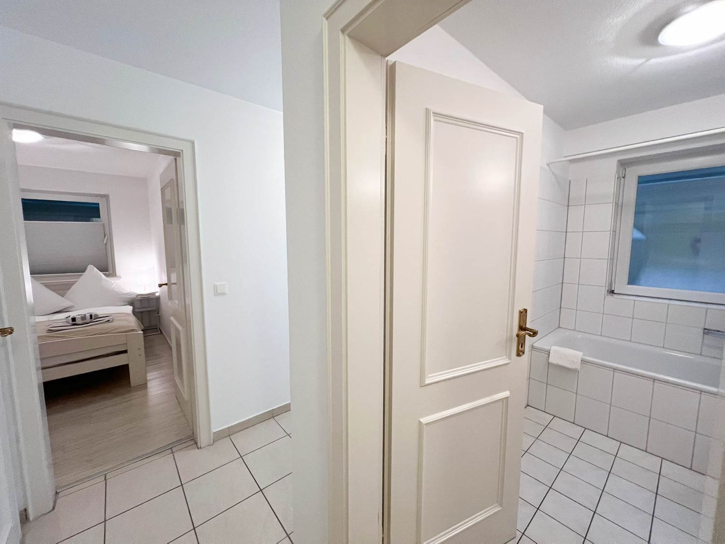 A hotel room with a bed, a bathroom with a window, and a door leading to another room.