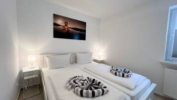 A hotel room with two beds, a nightstand with a lamp, a wall-mounted picture, and a window.