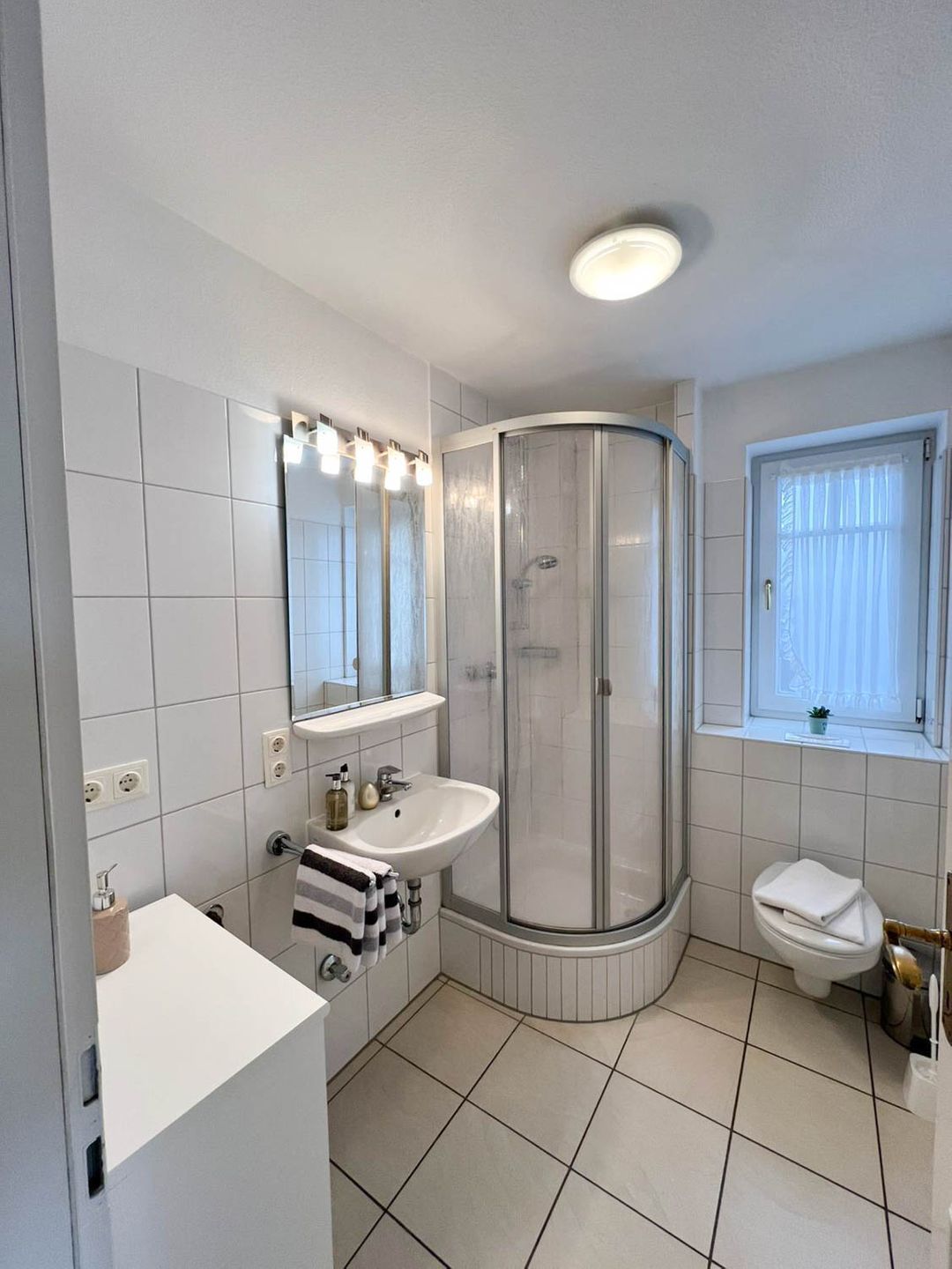 Un baño con lavamanos blanco, espejo y cabina de ducha.