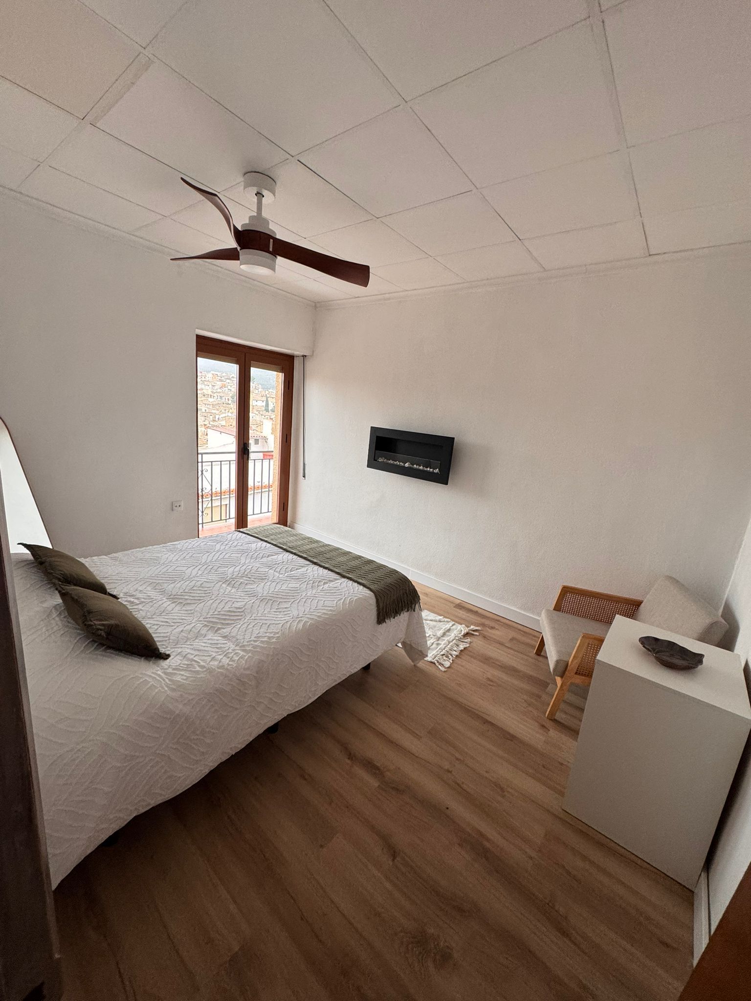 A bedroom with a bed, a ceiling fan, a TV, a desk, and a window with a view.