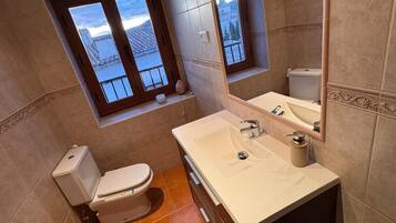 Un baño con inodoro, bidé, lavamanos y una ventana con vista a un edificio.