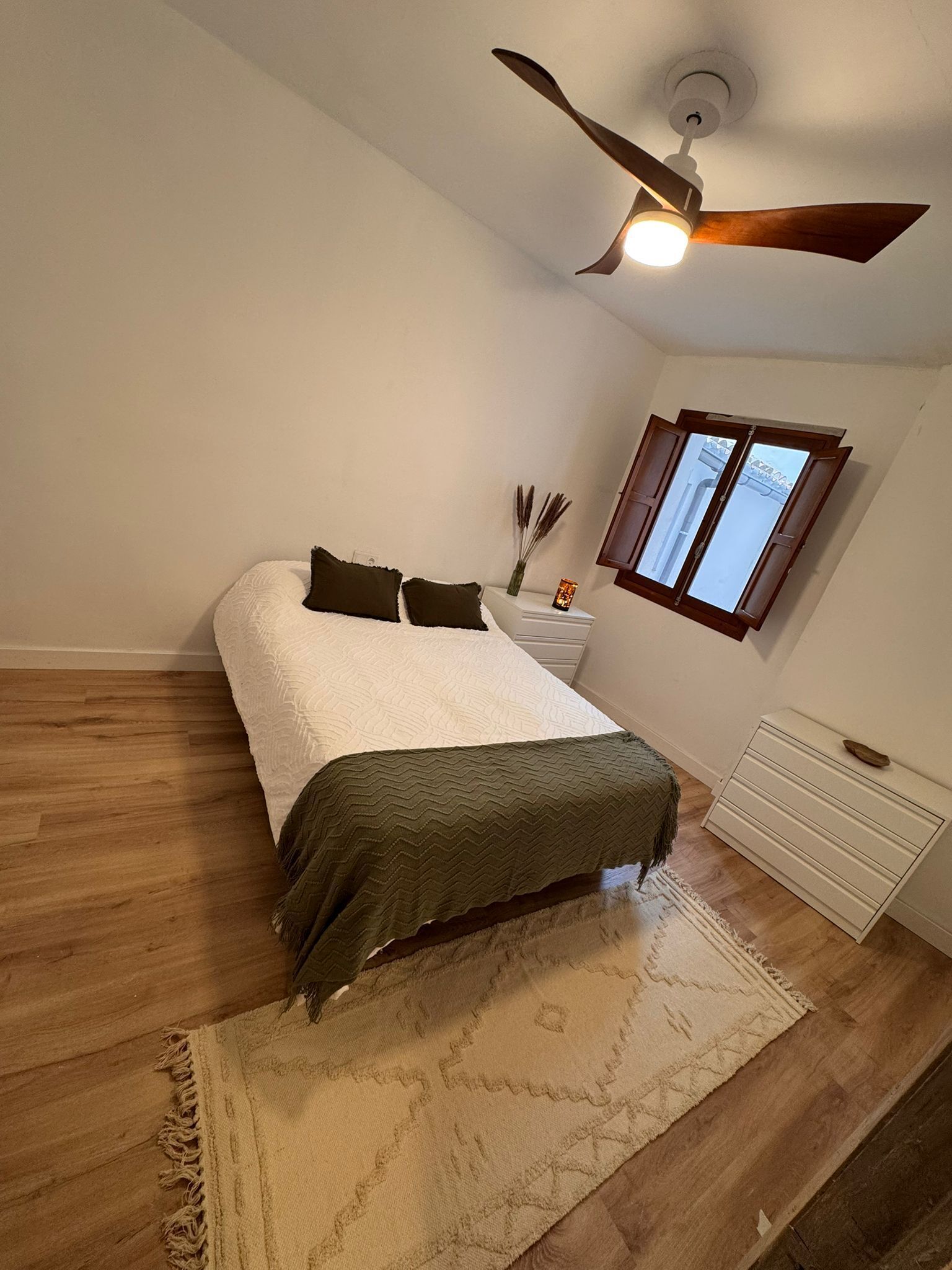 A bedroom with a bed, a nightstand, a dresser, a ceiling fan, and a window.