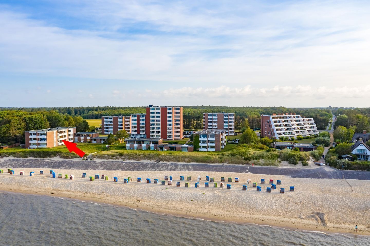 Ett hotell vid kusten med flera byggnader, en sandstrand och en klar himmel.