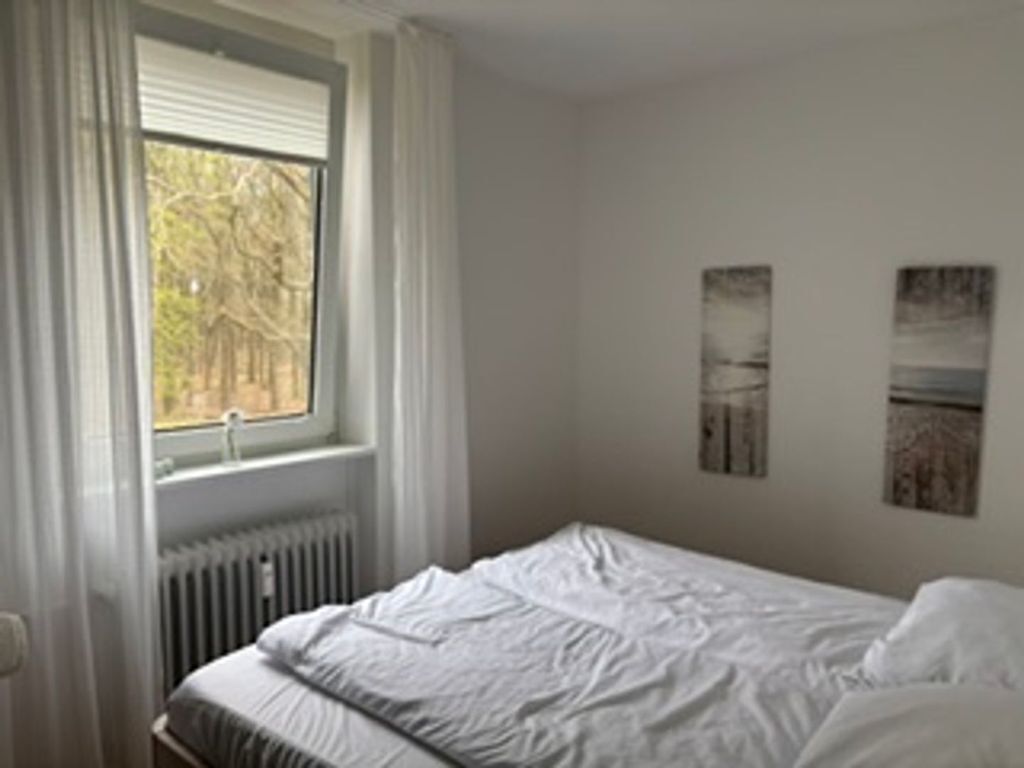 Un dormitorio con una cama, una ventana con cortinas y dos cuadros colgados en la pared.