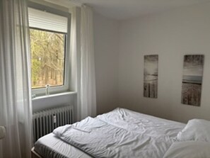 Een slaapkamer met een bed, een raam met gordijnen en twee foto's aan de muur.