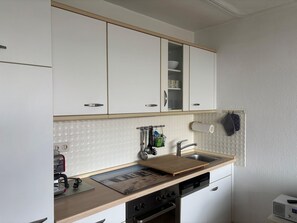 Een compacte keuken met witte kasten, een inbouwoven, een vaatwasser en een koffieapparaat.