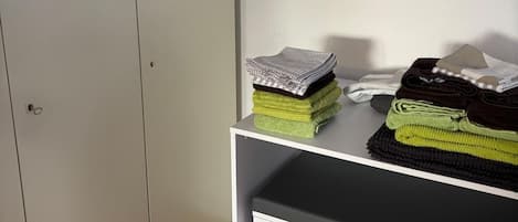 Une chambre avec un placard, un bureau où sont posées des serviettes et un tableau représentant un paysage marin.