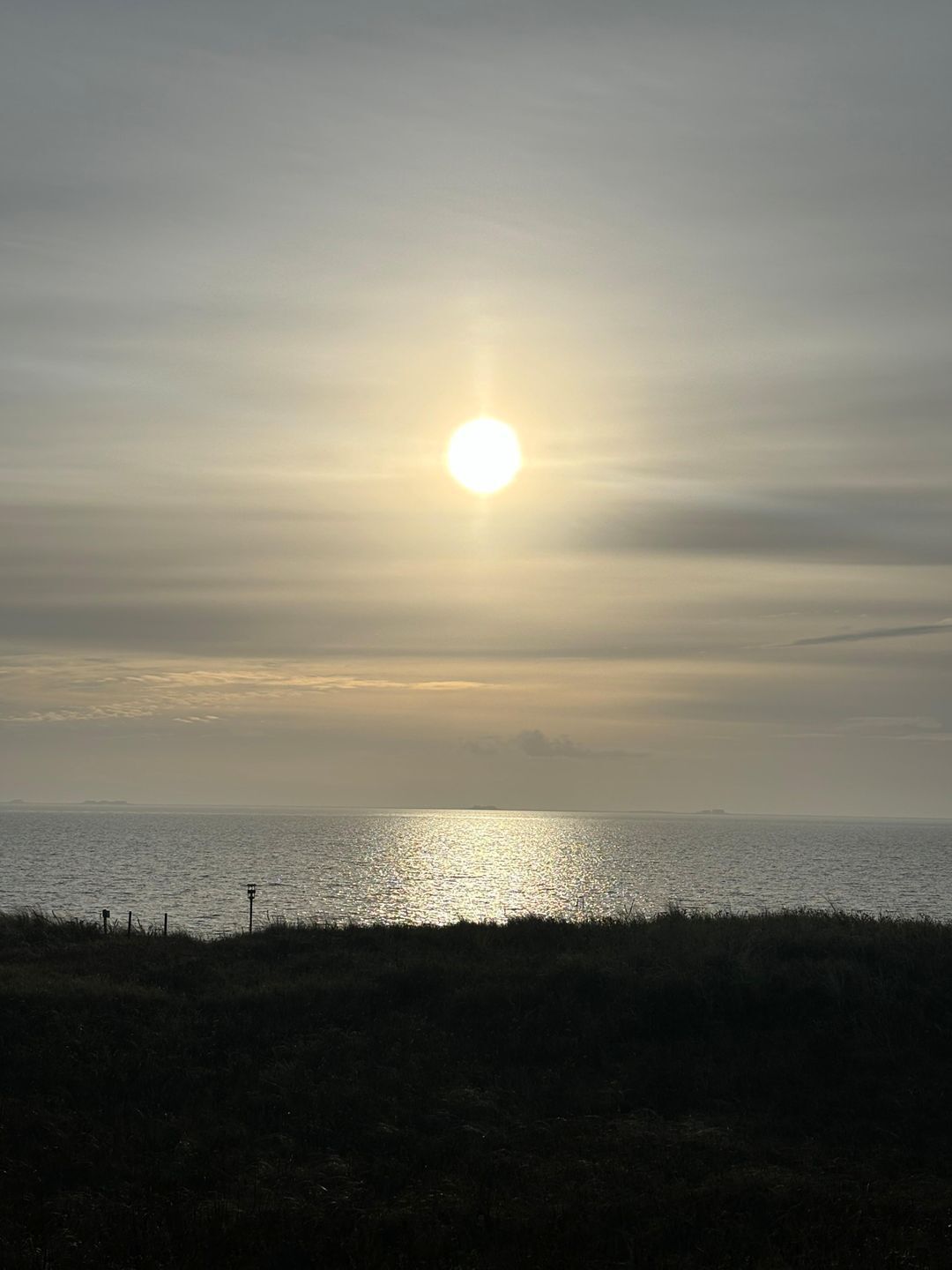 Una spiaggia con il sole basso all'orizzonte, che si riflette sull'acqua.