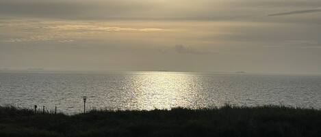 Una spiaggia con il sole basso all'orizzonte, che si riflette sull'acqua.