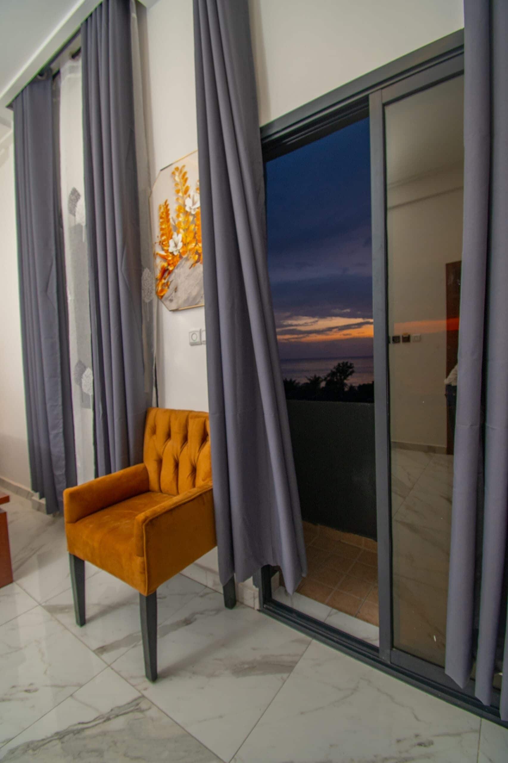 Ein Zimmer mit einer großen Schiebetür zum Balkon, einem einzelnen orangefarbenen Sessel und einem Wandbild.