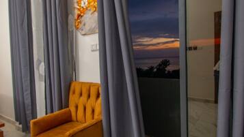 Ein Zimmer mit einer großen Schiebetür zum Balkon, einem einzelnen orangefarbenen Sessel und einem Wandbild.