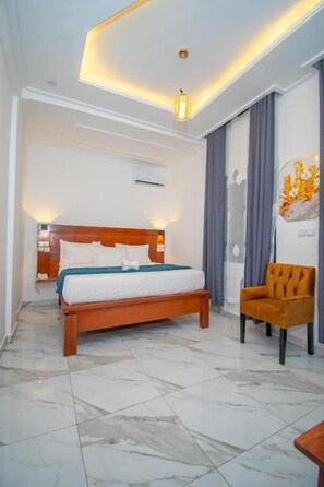 A hotel room with a bed, a chair, a wall-mounted air conditioner, and a ceiling light fixture.