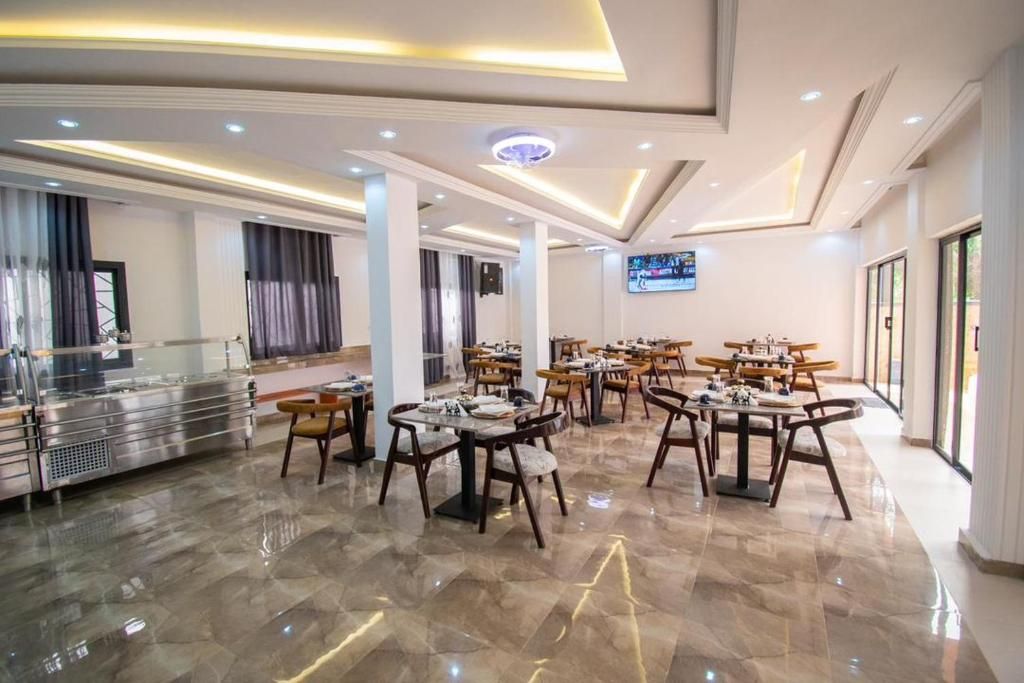 Un'ampia sala da pranzo dell'hotel con diversi tavoli e sedie, un banco buffet e uno schermo televisivo appeso al muro.