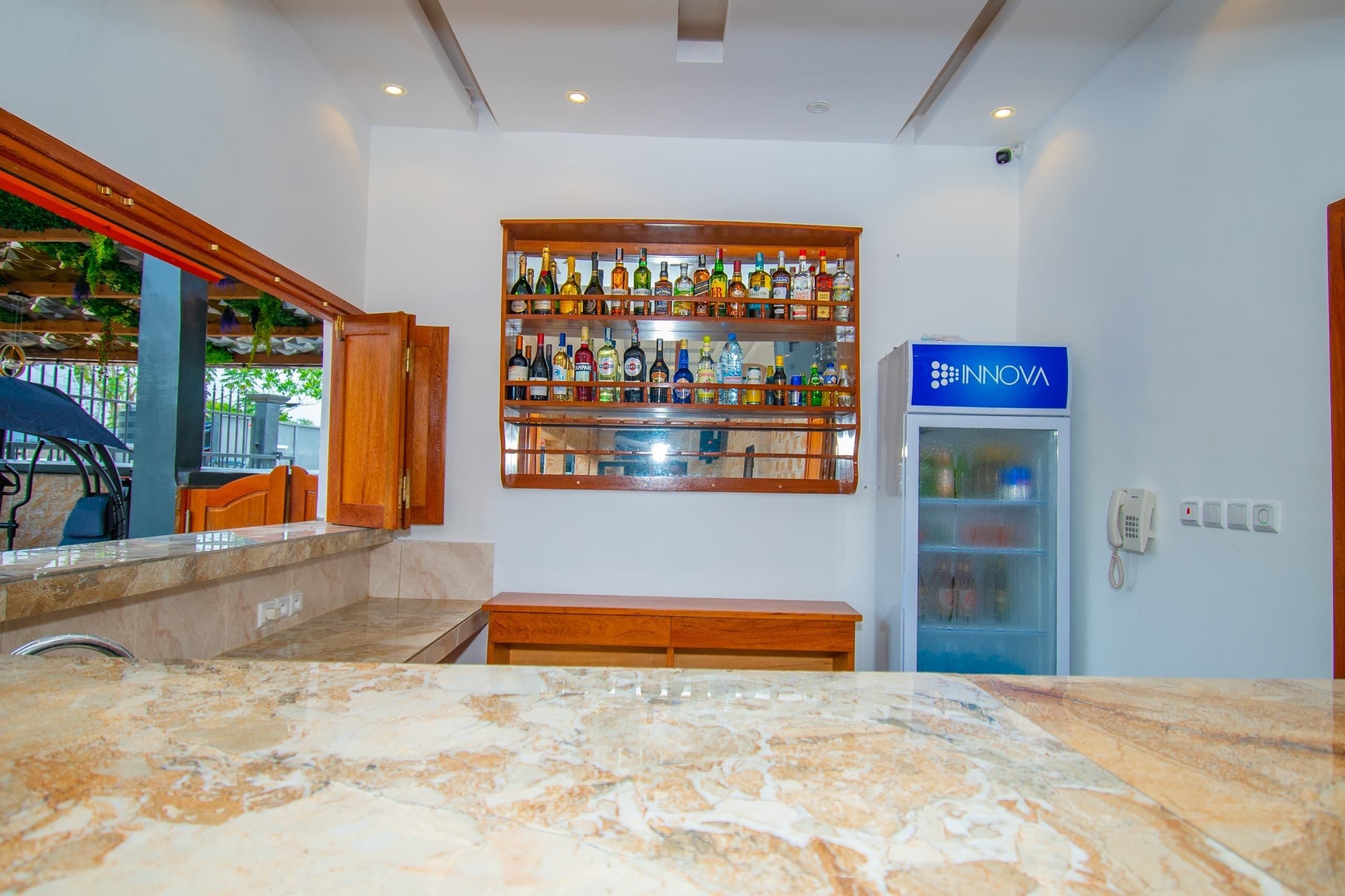 A bar area with a marble countertop, a wooden shelf with various bottles, and a blue refrigerator with the logo 'INOVA'.