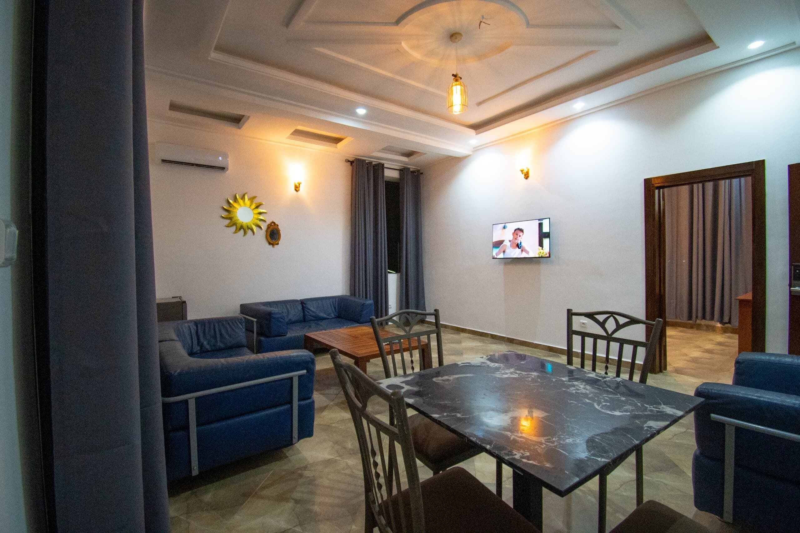 Sala de estar com sofá, cadeiras, mesa de centro, televisão e luminária no teto.