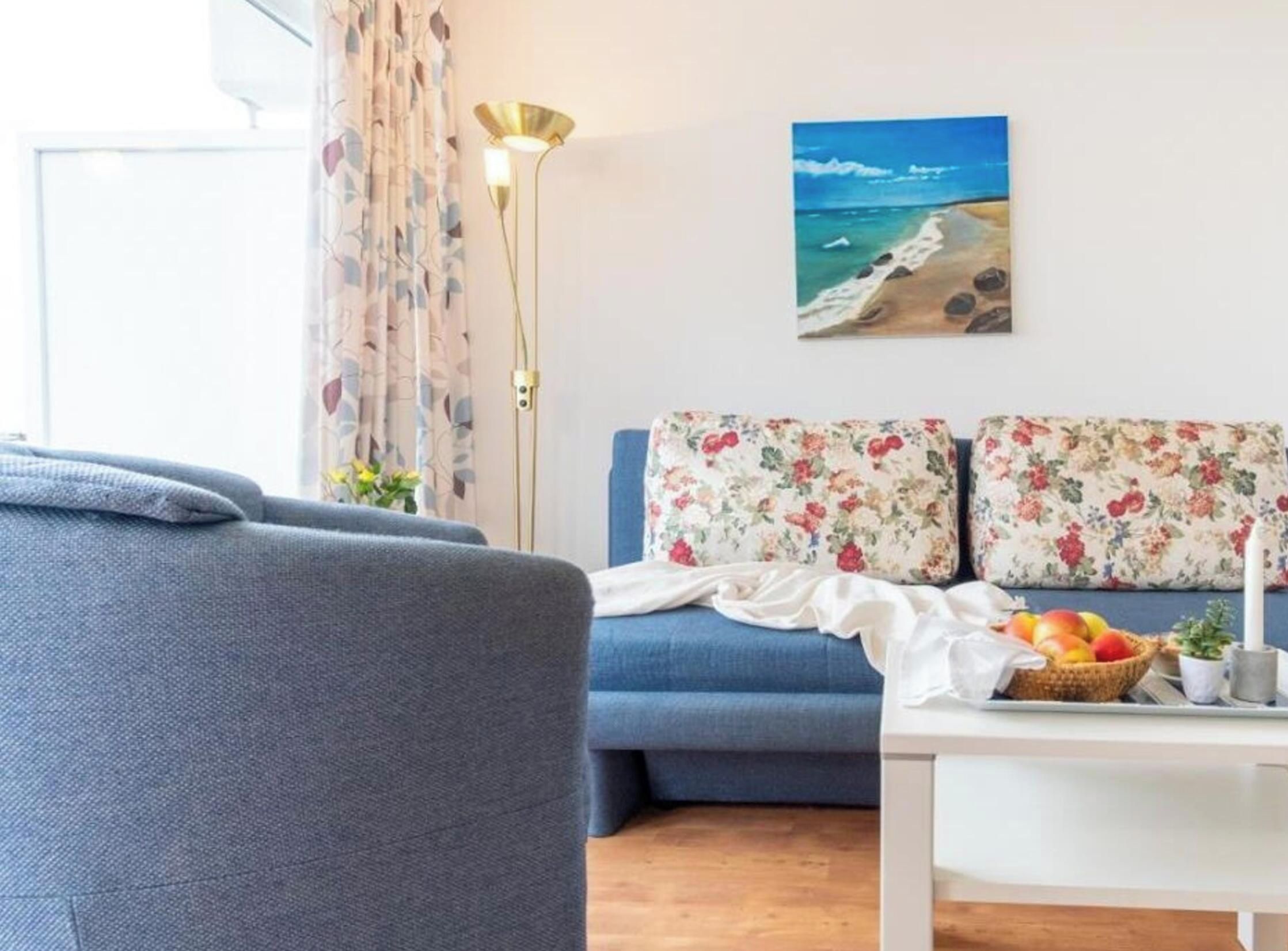 Un salon avec un canapé, une table sur laquelle on a disposé des fruits et un tableau représentant une plage.