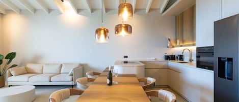 A modern kitchen with a central island, a dining area with a wooden table, and a seating arrangement with a sofa and chairs.