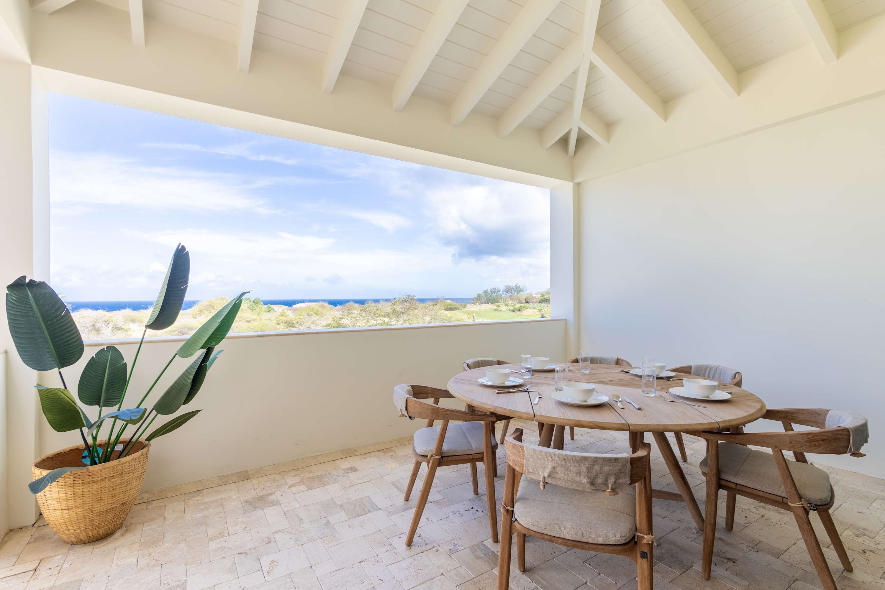A dining area with a large window overlooking a landscape, a round wooden table set for four, and a potted plant.