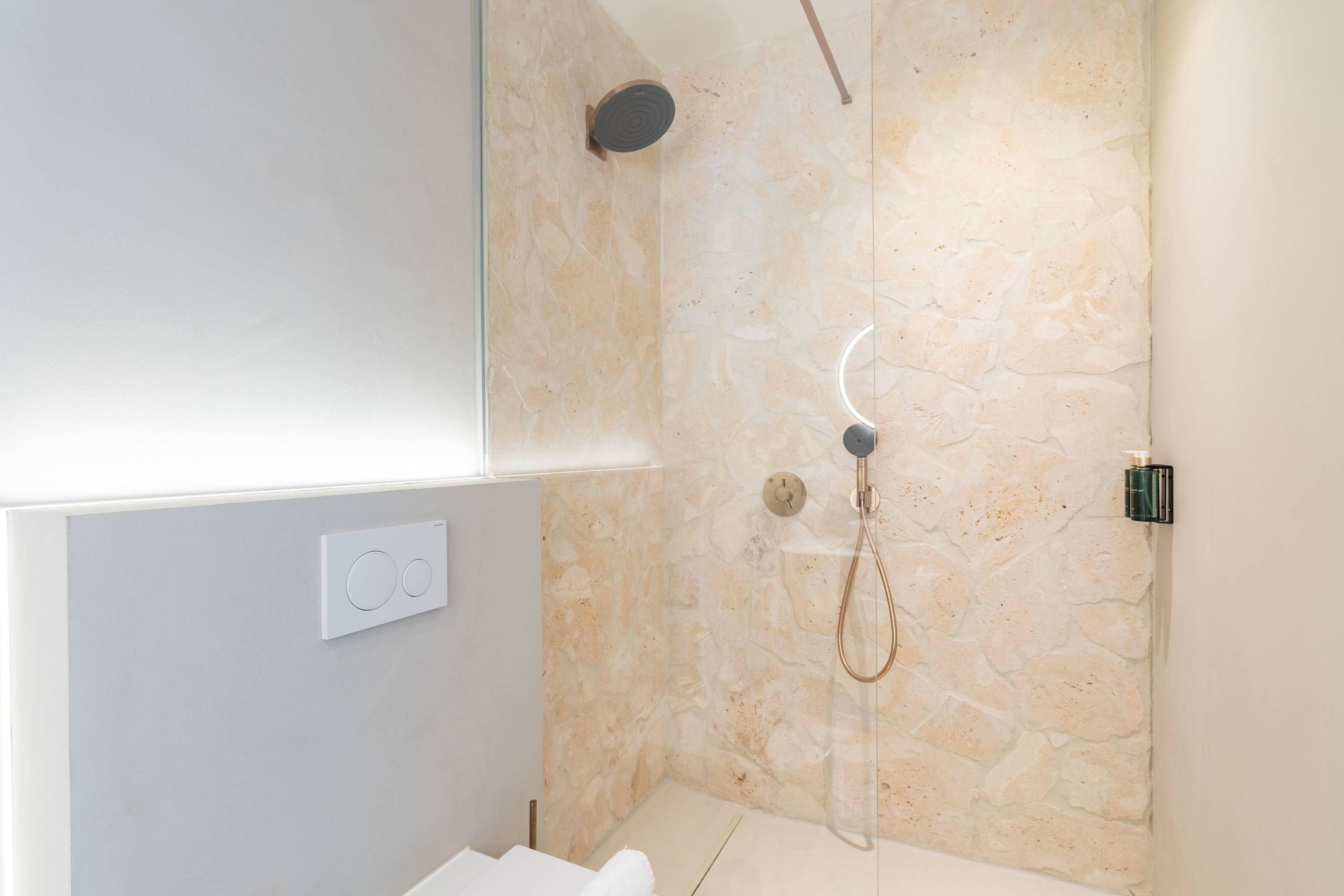 A modern bathroom with a stone shower wall, a handheld showerhead, and a built-in toilet.