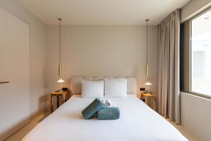Quarto de hotel com uma cama grande, duas mesas de cabeceira, uma janela com cortinas e parede com padrão.
