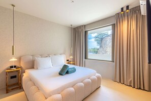 A bedroom with a large bed, two bedside tables, a window with curtains, and a view of the outdoors. - Sapphire at The Reef - Ocean View Penthouse (Sint Michiel)