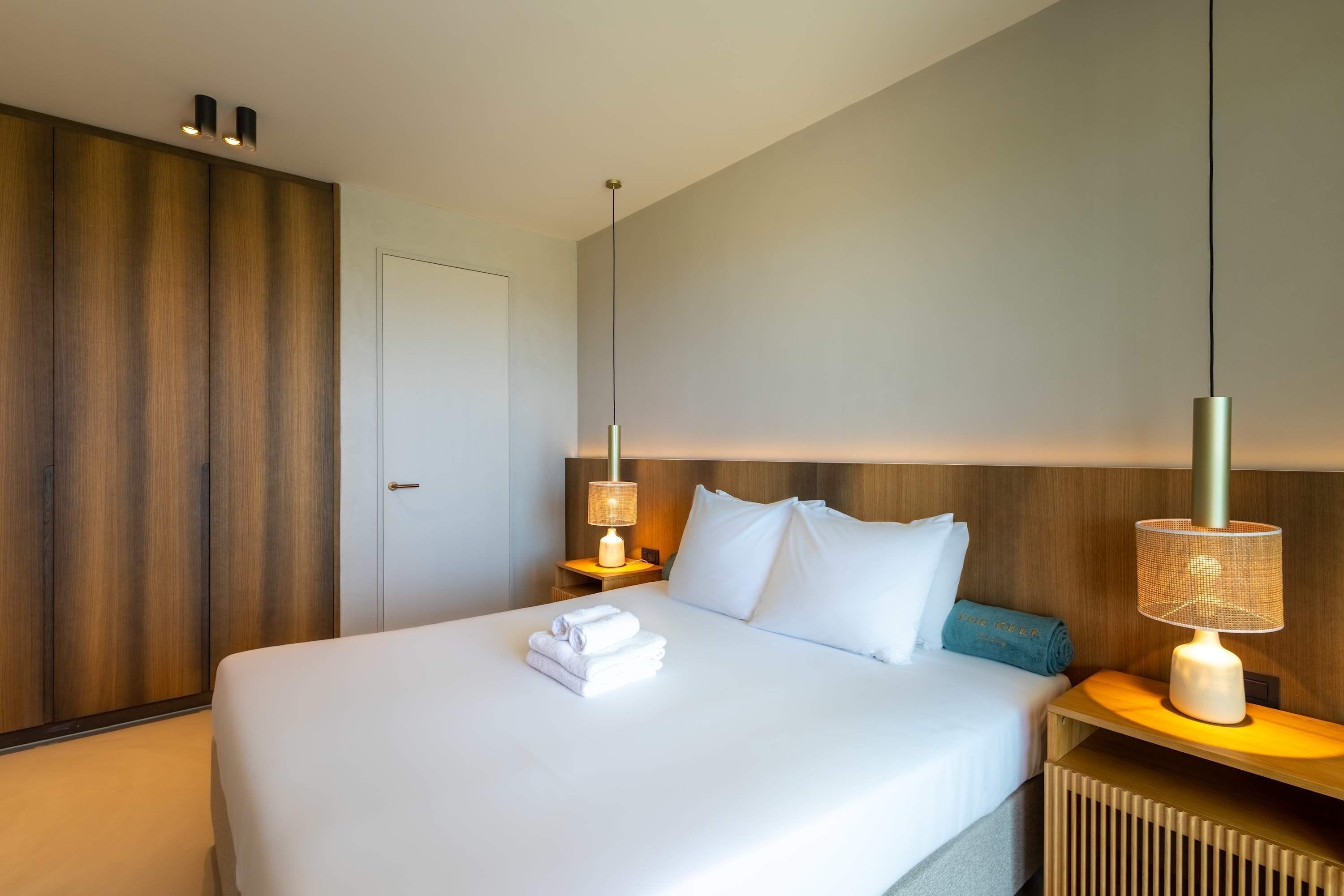 Une chambre d’hôtel avec un grand lit, deux lampes de chevet, une tête de lit en bois et un radiateur.