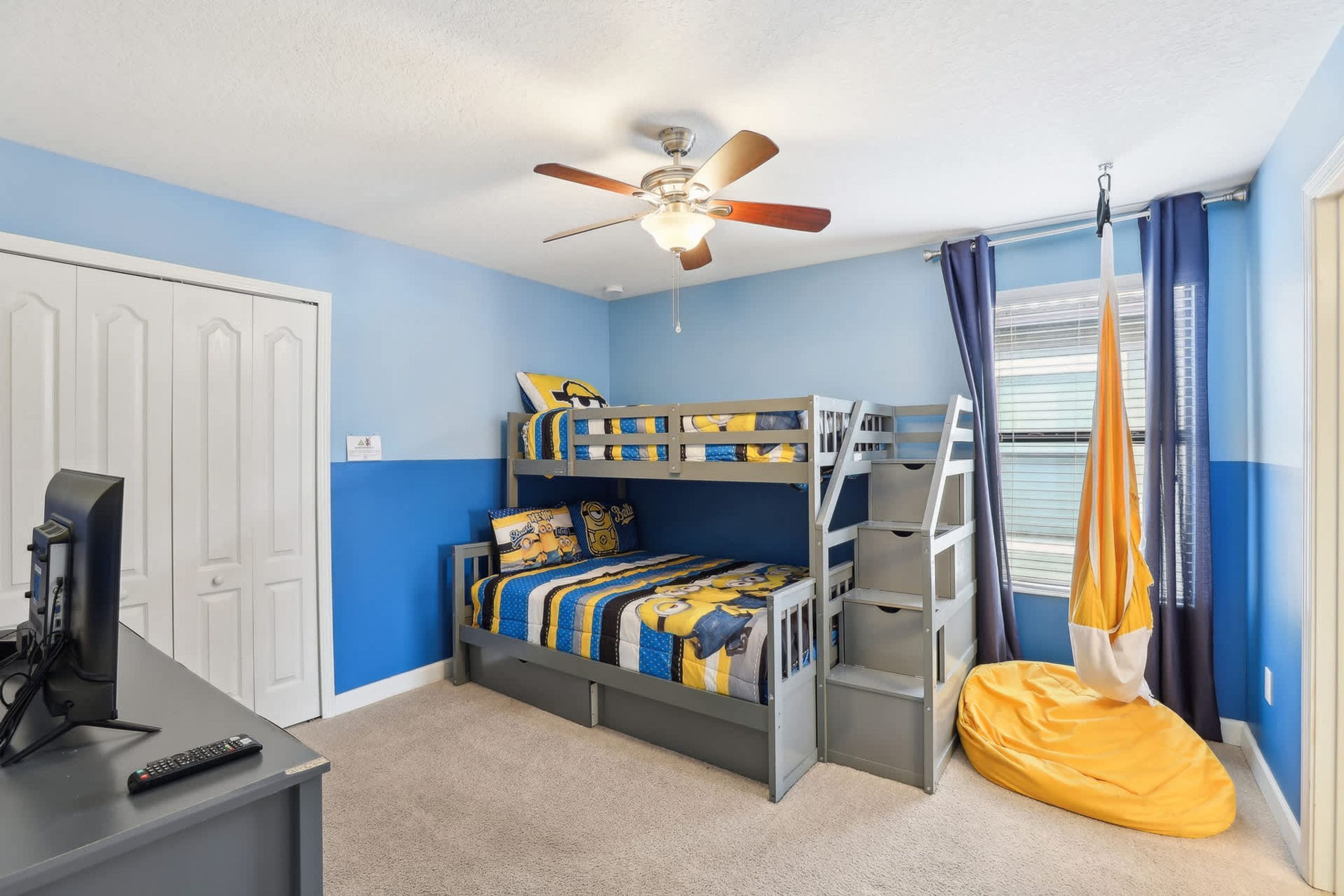 A bedroom with a bunk bed, a desk with a computer, a hanging chair, and a ceiling fan.