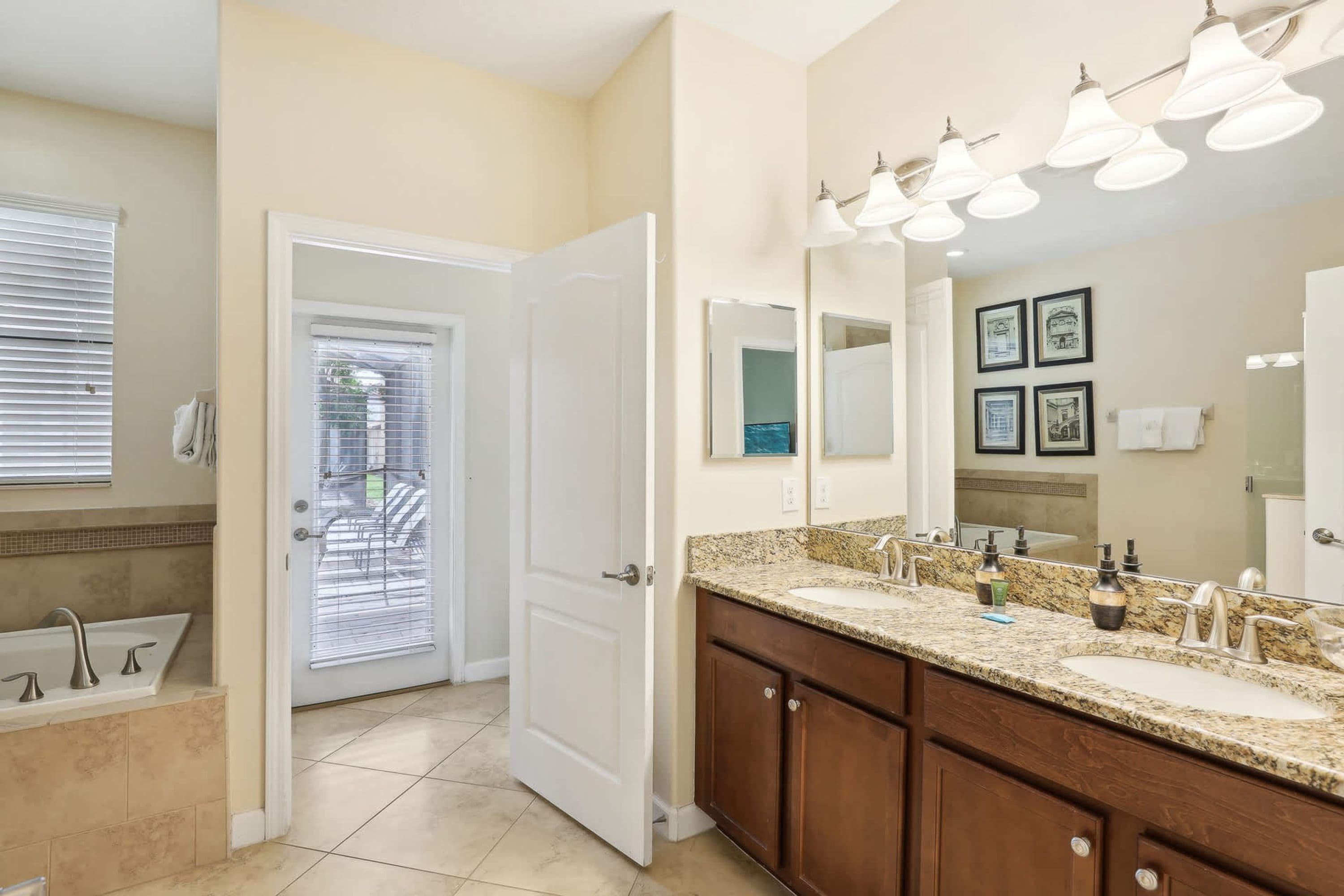 A bathroom with a double sink vanity, a large mirror, and a door leading to a balcony.