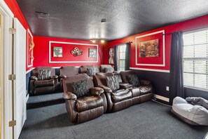 Une salle de cinéma maison aux couleurs rouge et noir, avec des canapés inclinables en cuir et des affiches accrochées aux murs.