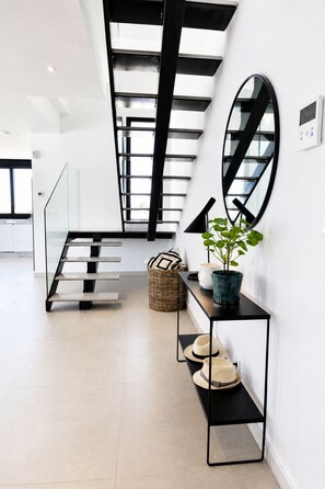 A modern interior with a staircase, a console table with a potted plant, and a wall-mounted mirror. - Exclusive Villa in Campoamor by NRAS (Dehesa de Campoamor)