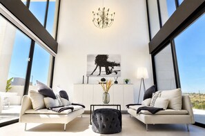 A modern living room with two sofas, a chandelier, a painting, and a view through large windows. - Exclusive Villa in Campoamor by NRAS (Dehesa de Campoamor)