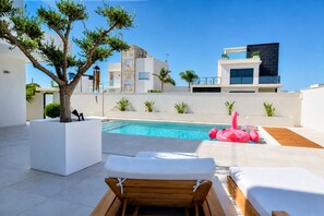 A rooftop pool area with lounge chairs, a tree, and modern buildings in the background. - Exclusive Villa in Campoamor by NRAS (Dehesa de Campoamor)