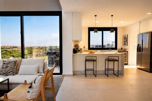 A modern kitchen with a large island, bar stools, and a view of the city. - Exclusive Villa in Campoamor by NRAS (Dehesa de Campoamor)