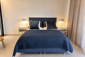 A bed with a dark blue quilted bedspread, two bedside tables with lamps, and a wooden chair. - Exclusive Villa in Campoamor by NRAS (Dehesa de Campoamor)