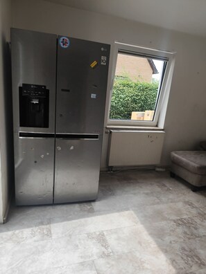 A compact kitchen with a stainless steel refrigerator, a window with a view of greenery, and a tiled floor.