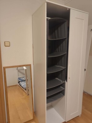 A white wardrobe with multiple shelves, a mirror, and a door.