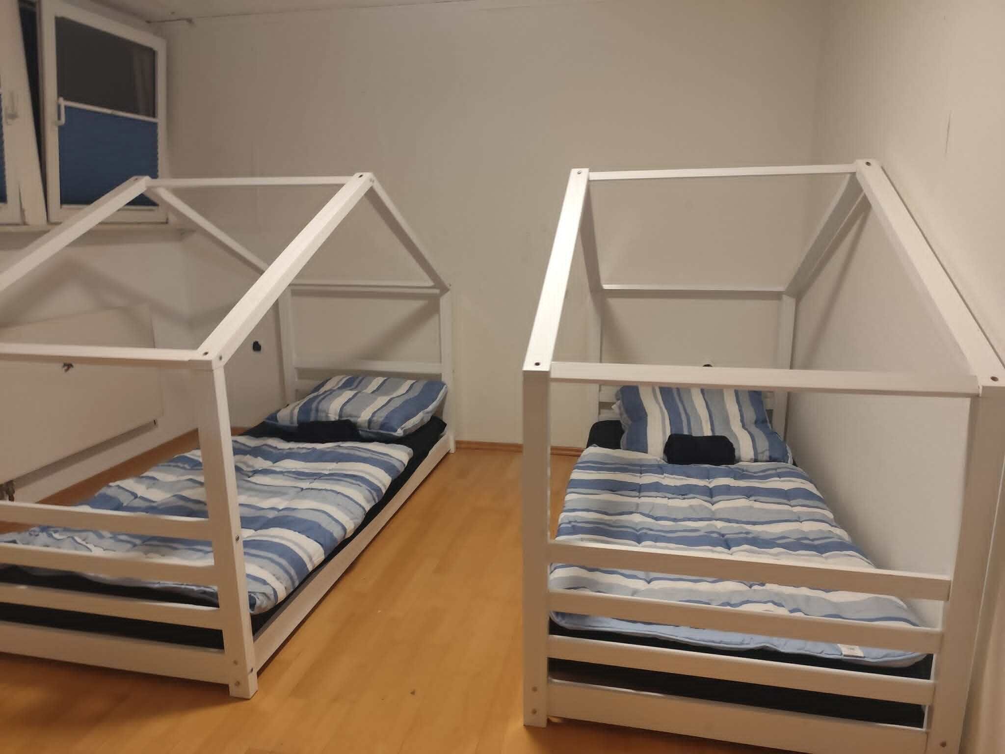 Two bunk beds with a white frame, a window with blue blinds, and a wooden floor.