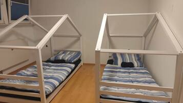 Two bunk beds with a white frame, a window with blue blinds, and a wooden floor.