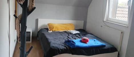 A bedroom with a bed, a coat rack, a window, and a radiator.